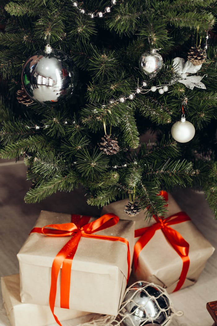 Festive Christmas tree adorned with silver ornaments and gifts wrapped in red ribbon.